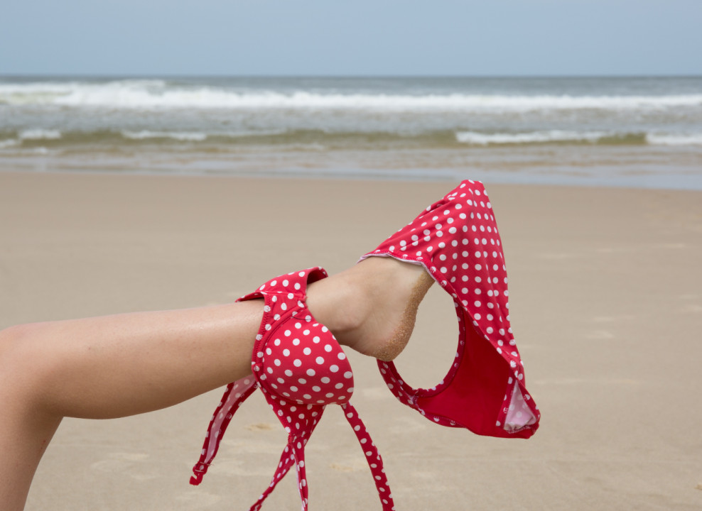 На ноге висит купальник, фото на фоне моря. Источник: Adobe Stock